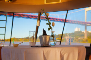Mariage en bateau Vue intérieure du Burdigala 2 avec une table décorée pour un mariage, comprenant un vase en verre rempli de roses, quelques décorations et un emballage traiteur, illustrant l'aménagement possible pour un événement à bord.